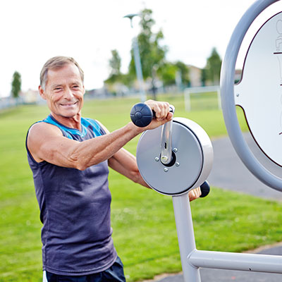 A man is working out at an outdoor gym, looking directly at the camera and smiling.